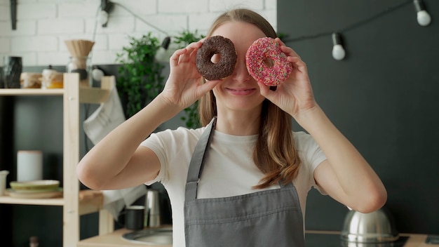 Glückliche Frau in der Schürze hält Donuts vor ihren Augen in der Küche
