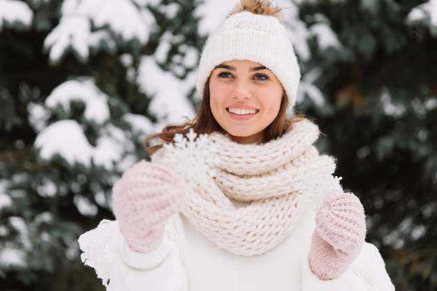 Glückliche Frau in der weißen Winterkleidung, die eine schöne Schneeflocke in einem Park hält.