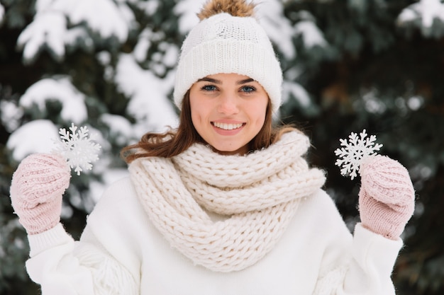 Glückliche Frau in der weißen Winterkleidung, die eine schöne Schneeflocke in einem Park hält.