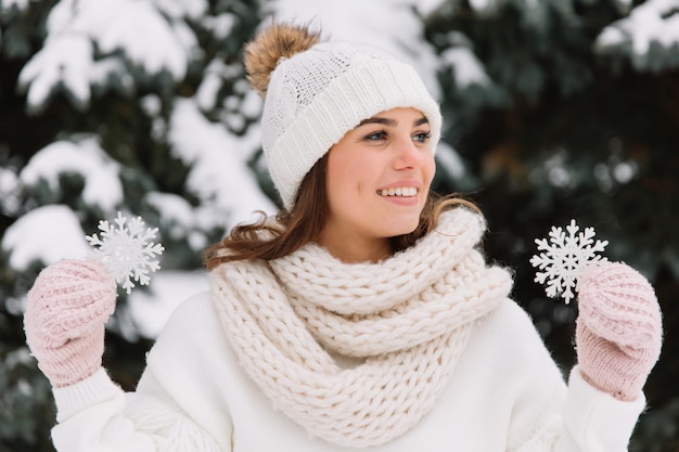 Glückliche Frau in der weißen Winterkleidung, die eine schöne Schneeflocke in einem Park hält.