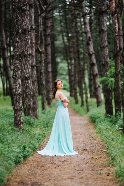 Glückliche Frau in einem türkisfarbenen langen Kleid in einem grünen Park