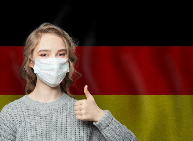 Glückliche Frau in einer Gesichtsmaske, die den Daumen auf der Nationalflagge hält Deutschland Hintergrund Grippe-Epidemie und Virus-Schutzkonzept