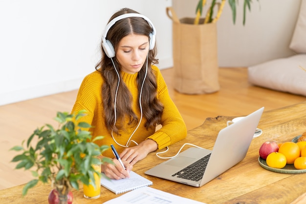 Glückliche Frau in kabellosen Kopfhörern, die Online-Kurs studieren, PC verwenden und in Notizblock schreiben, Speicherplatz kopieren