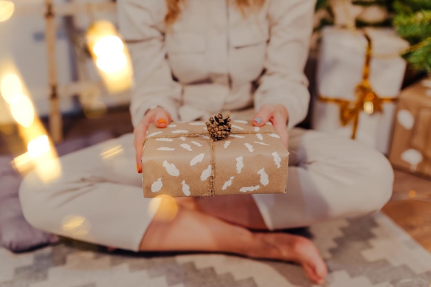 Glückliche Frau in Sankt-Hut mit Weihnachtsgeschenk in den Händen. Frau, die unter Weihnachtsbaum sitzt.