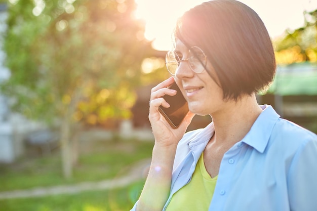 Glückliche Frau mit Brille, die am Handy im Freien spricht