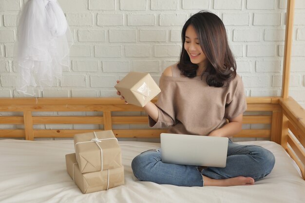 Glückliche Frau mit Computer- und Produktpaketbox zu Hause arbeiten zu Hause Warenlieferungskonzept