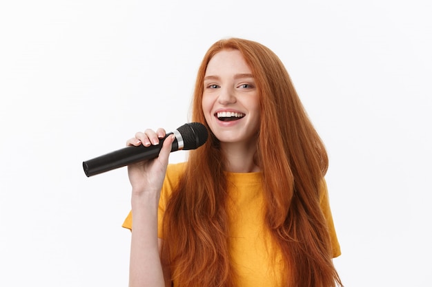 glückliche Frau mit dem lockigen Haar, das singt, während Mikrofon über Weiß isoliert hält