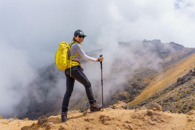 Glückliche Frau mit einem gelben Rucksack, der lächelt, nachdem sie an einem nebligen Tag auf Iztaccihuatl Mexiko gewandert ist