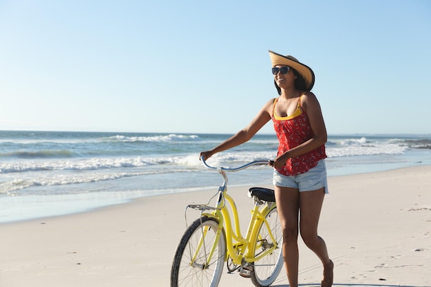 Glückliche Frau mit gemischter Abstammung im Strandurlaub, die mit dem Fahrrad spaziert. Freizeiturlaub im Freien am Meer.