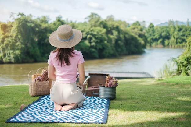 Glückliche Frau mit Hut in Picknickzeit im Park in der Nähe des Flusses Sommerfrühling und Urlaubskonzept