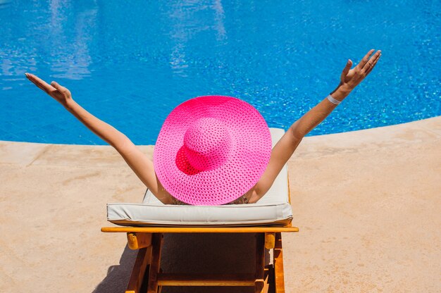 Glückliche Frau mit Hut Sonnenbaden auf einer Sonnenliege am Pool