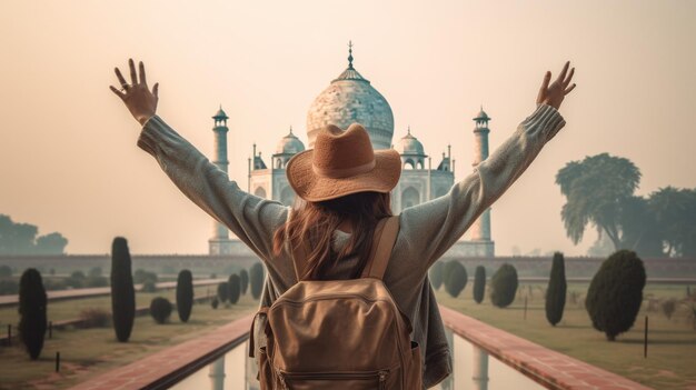 Glückliche Frau mit Hut und Rucksack hebt ihre Arme gegen den Hintergrund des Taj Mahal