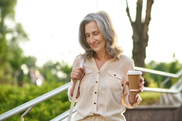 Glückliche Frau mit Kaffee im Park spazieren gehen