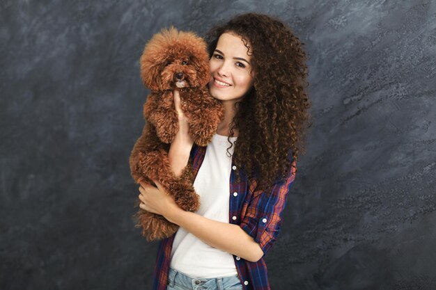 Glückliche Frau mit kleinem Hund, Porträt am grauen Hintergrund. Zwei schöne Locken posieren im Studio, Kopierraum