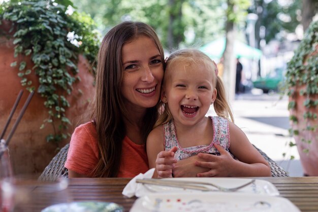 Glückliche Frau mit kleinen blonden Mädchen an einem Tisch auf einer Sommerterrasse der Cafeteria.