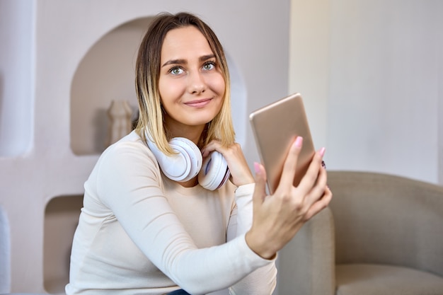 Glückliche Frau mit Kopfhörern macht Videoanruf im Wohnzimmer