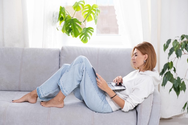 Glückliche Frau mit Laptop-Computer-Gerätetechnologie, die zu Hause auf der Couch sitzt