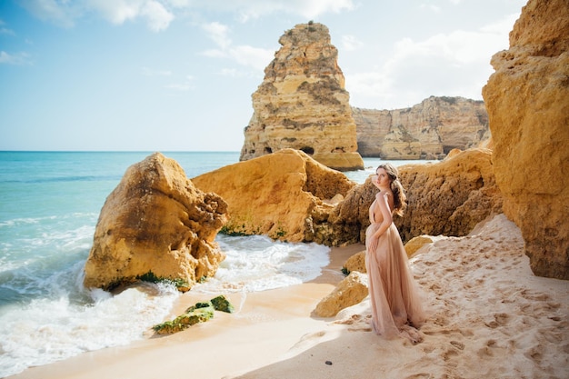 glückliche Frau mit Rücken in einem gelben Kleid, die bei Sonnenuntergang am Strand und am Meer steht