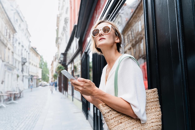 Glückliche Frau mit Smartphone auf der Straße einer europäischen Stadt Moderne Lebensweise der städtischen Menschen