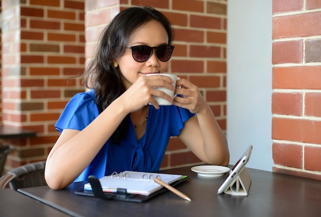 Foto glückliche frau mit sonnenbrille trinken im café