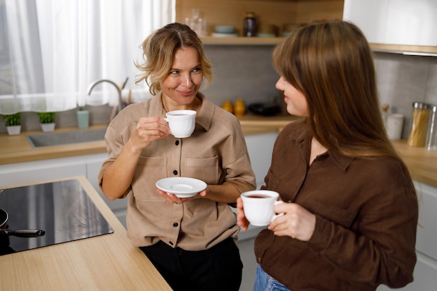 Glückliche Frau mittleren Alters, die mit ihrer erwachsenen Tochter in der Küche Kaffee genießt