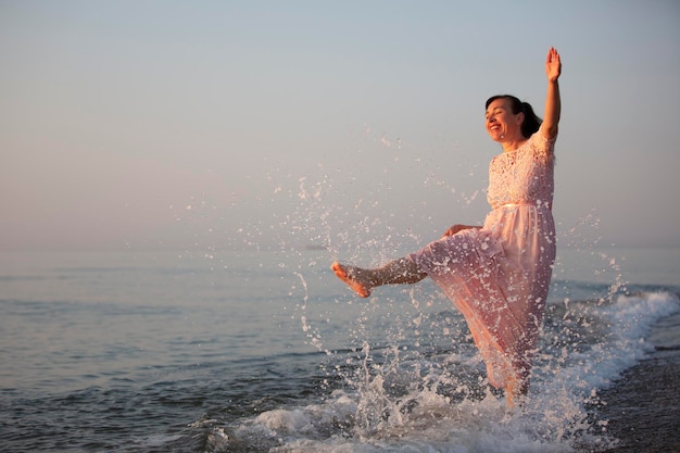 Glückliche Frau mittleren Alters in einem Kleid spritzt Wasser am Meer