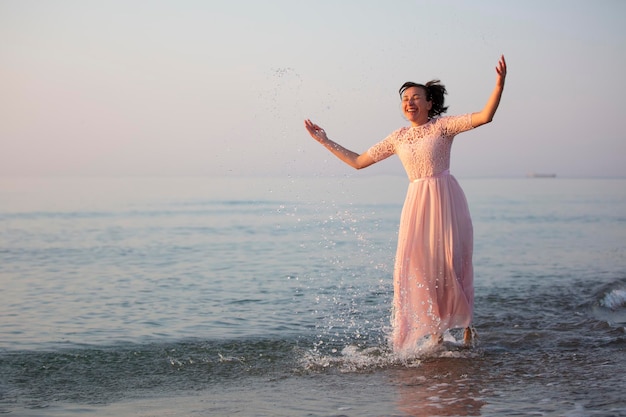 Glückliche Frau mittleren Alters in einem Kleid spritzt Wasser am Meer