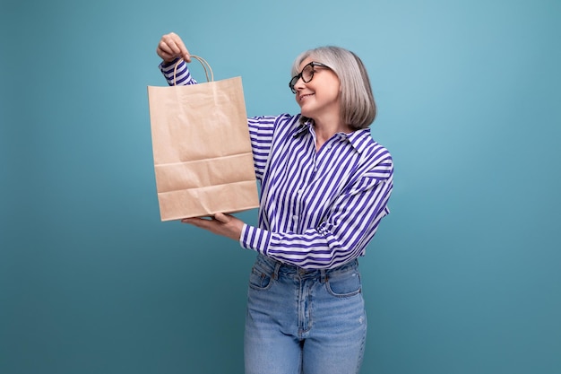 Glückliche Frau mittleren Alters mit grauem Haar in einem stilvollen Look, die eine Basteltasche mit einem Einkauf auf a hält