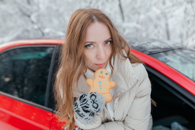 Glückliche Frau schaut aus dem Autofenster, hält einen Keks in Form eines Mannes in den Händen. Winterwald.