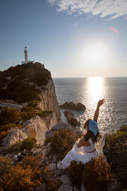 Glückliche Frau sitzt auf der Klippe Blick auf den Sonnenuntergang der Insel Lefkada Leuchtturm über dem Meer Griechenland