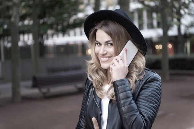 Glückliche Frau spricht über Handy in Paris, Frankreich. Sinnliche Frau mit langen blonden Haaren, Frisur, Schönheit. Modernes Leben, neue Technologie, mobiles Gerät. Mode, Stil, Accessoire. Schönheit, Aussehen, Make-up.