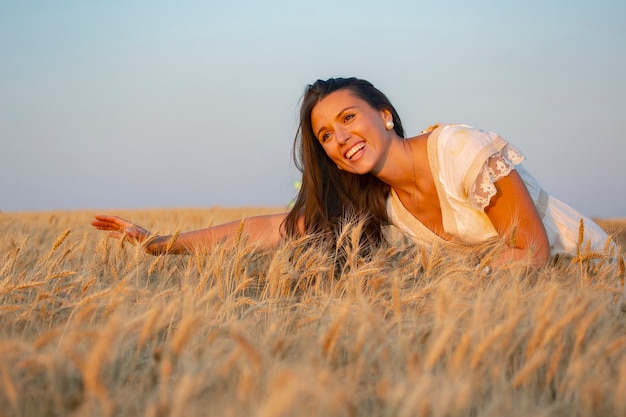 Glückliche Frau steht im Sommer auf einem Weizenfeld vor dem Hintergrund einer untergehenden Sonne