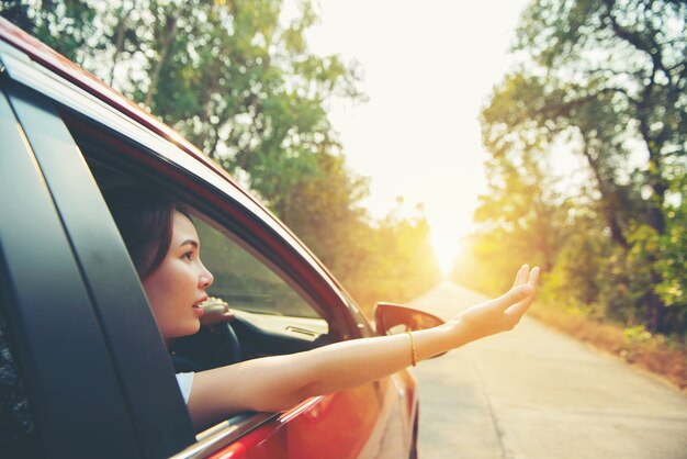 Glückliche Frau teilt Fensterauto rot mit Sonnenlicht aus