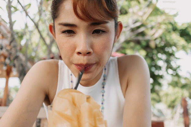 Glückliche Frau trinkt Mangosaft-Smoothie am Sommertag