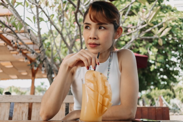 Glückliche Frau trinkt Mangosaft-Smoothie am Sommertag