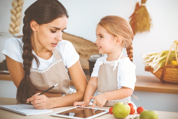 Glückliche Frau und ihre Tochter suchen nach neuen Rezepten für eine sonnige Familienküche