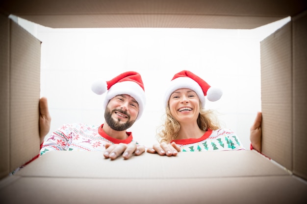 Glückliche Frau und Mann, die den Kasten untersuchen. Lustiges überraschtes Paar packen Weihnachtsgeschenkbox aus. Weihnachtsferienkonzept. Niedrigwinkelansicht.