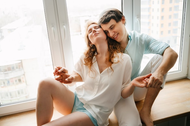 Glückliche Frau und Mann, die nahe Fenster im Haus am Valentinstag umarmen