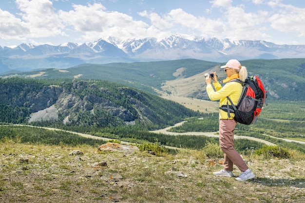 Glückliche Frau Wanderer stehen am Hang des Bergrückens gegen Berge blauer bewölkter Himmel im Hintergrund Wandernde Frau, die Bilder mit Digitalkamera macht