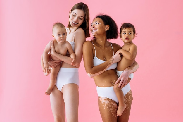 Glückliche Frauen, die ihre Babys auf farbigem Hintergrund halten - Junge Frauen, die Unterwäsche tragen und sich um ihre kleinen Söhne kümmern - Schwangerschaft, Mutterschaft, Menschen und Erwartungskonzept