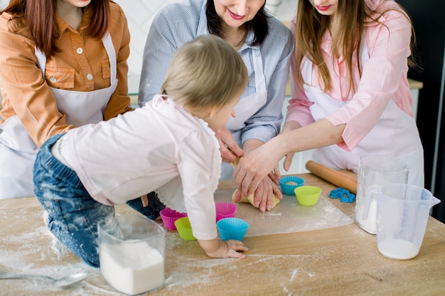 Glückliche Frauen in weißen Schürzen, die zusammen backen. Nahaufnahmefoto von Frauenhänden und kleinem Baby, das Teig zum Backen von Muffins vorbereitet. Familien-, Koch-, Back- und Personenkonzept