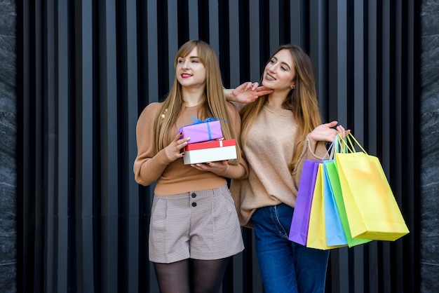 Glückliche Frauen mit Geschenken und Einkaufstüten, die auf der Stadtstraße spazieren. Neujahrs- und Weihnachtsfeierkonzept