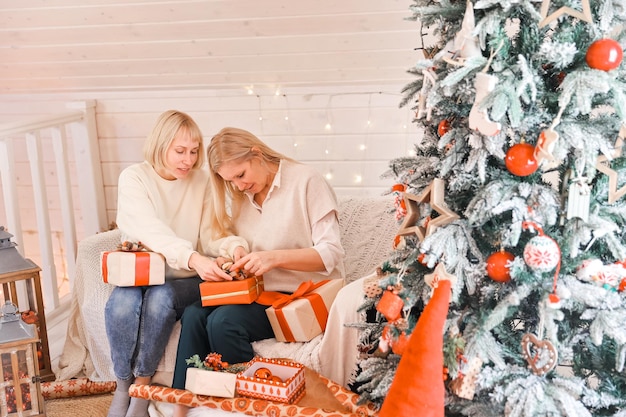 Glückliche frauenmütter bereiten sich auf weihnachten vor, neujahrsgeschenke zu hause, während sie in der nähe des weihnachtsbaums sitzen. winterurlaub, dekorationskonzept