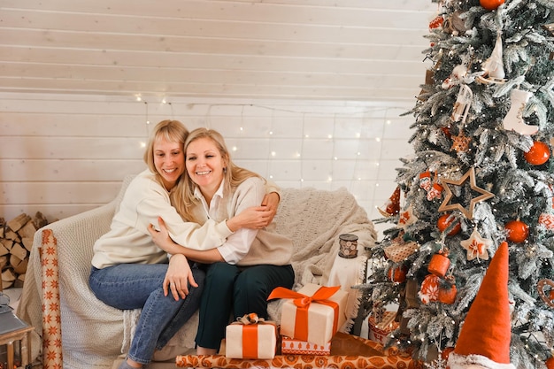 Glückliche Frauenmütter bereiten sich auf Weihnachten vor, Neujahrsgeschenke zu Hause, während sie in der Nähe des Weihnachtsbaums sitzen. Winterurlaub, Dekorationskonzept