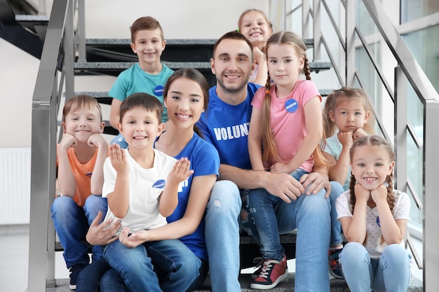 Glückliche Freiwillige und Kinder, die drinnen auf Treppen sitzen