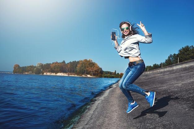 Glückliche freudige Frau, die Musik hört, während sie im Freien nahe dem Meer ist