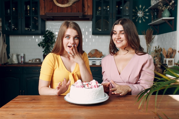 Glückliche Freunde der Frauen zu Hause, die mit weißem Geburtstagskuchen sitzen und lächeln