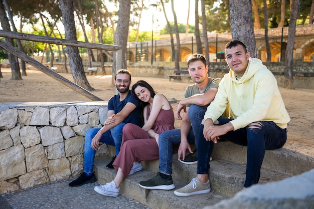 Glückliche Freunde, die auf den Stufen eines Parks mit Kiefern sitzenSie schauen lächelnd in die Kamera