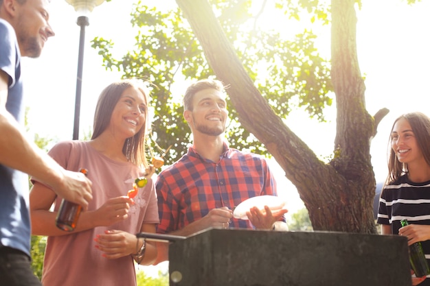 Glückliche Freunde, die Fleisch grillen und eine Grillparty im Freien genießen.