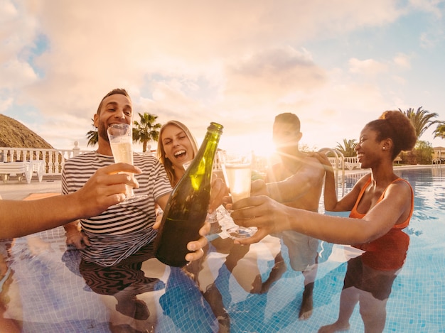 Foto glückliche freunde, die mit champagner in der poolparty bei sonnenuntergang jubeln